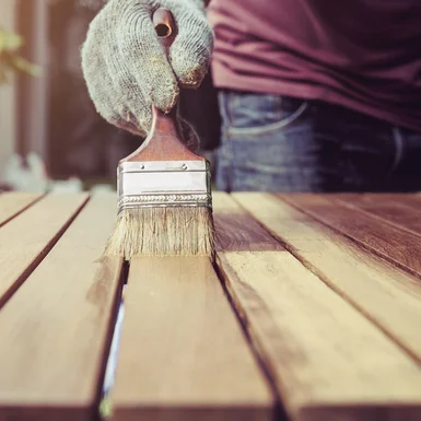 Person streicht Holz mit Pinsel.