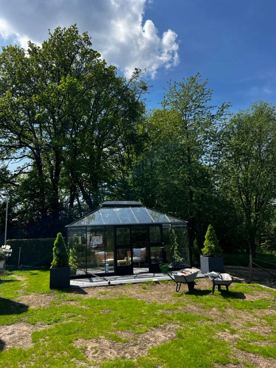 Ein modernes, schwarzes Glashaus in einem Garten, davor stehen zwei Schubkarren.