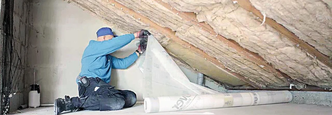 Person bringt Dämmfolie an Dachschräge an