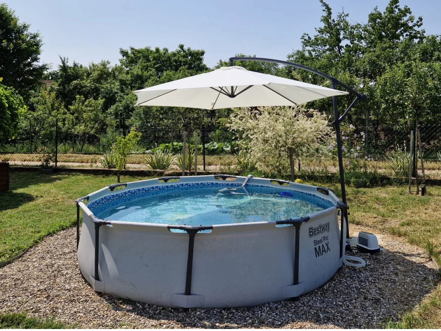 Ein runder Aufstellpool mit einem großen Sonnenschirm in einem sommerlichen Garten.