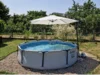 Ein runder Aufstellpool mit einem großen Sonnenschirm in einem sommerlichen Garten.