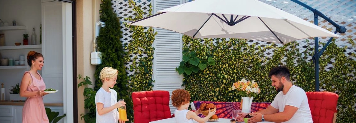 Eine Familie isst gemeinsam draußen unter einem Sonnenschirm.