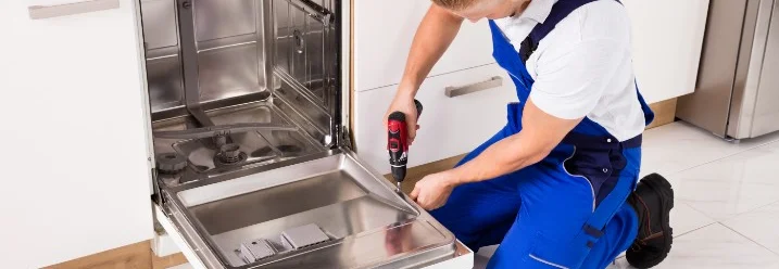 Person repariert Geschirrspüler mit Akkuschrauber.