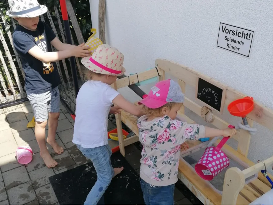 Drei Kinder spielen an einer Matschküche