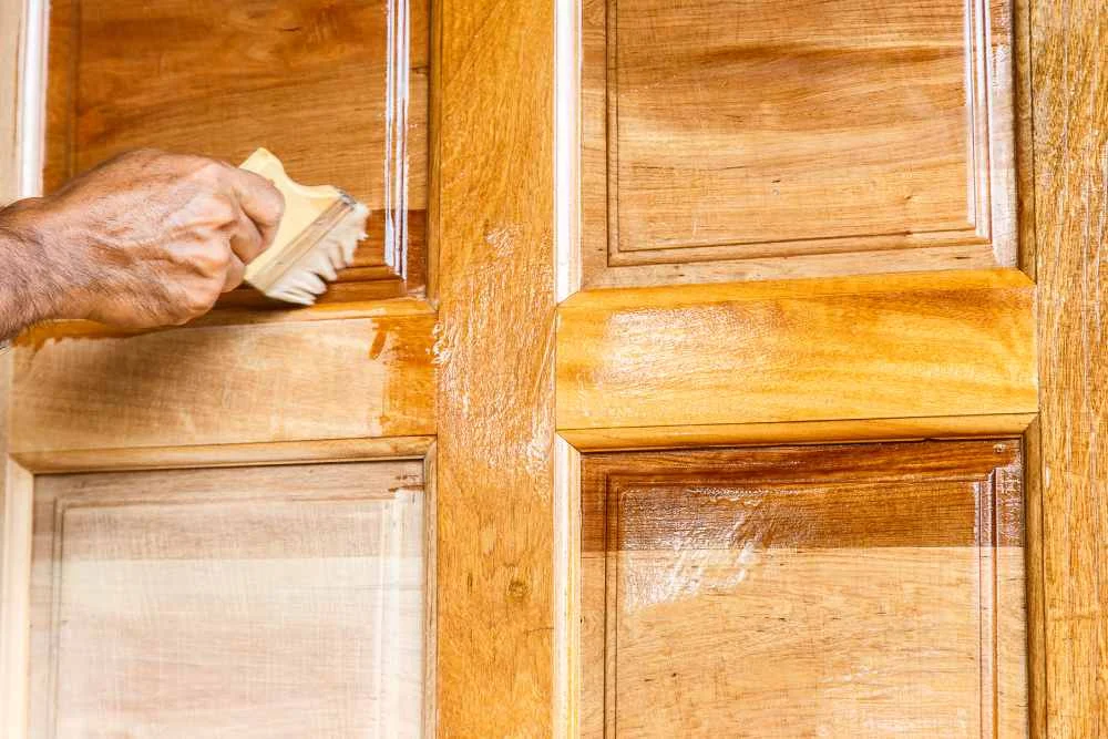 Person lasiert eine Tür mit einem Pinsel.