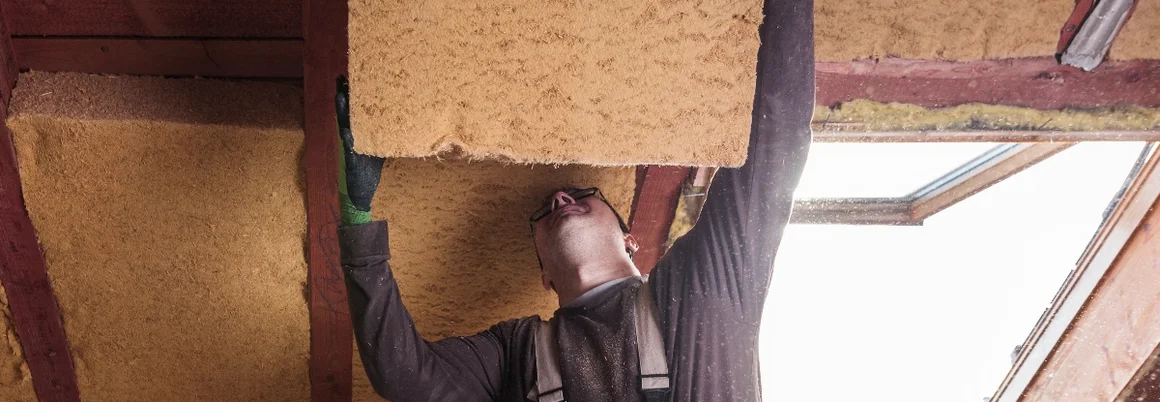 Person setzt Dämmmaterial unterm Dach ein