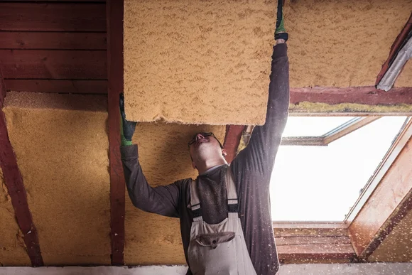 Person setzt Dämmmaterial unterm Dach ein