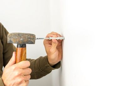 Nageldübel wird mit Hammer an Wand angebracht