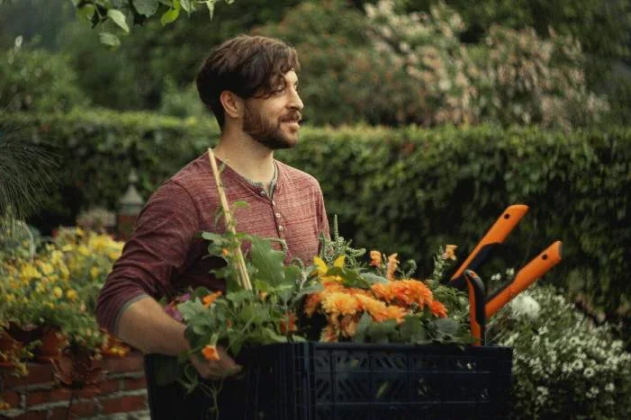 Person trägt Kiste mit Blumen und Gartenschere