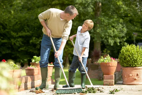 Zwei Personen kehren Blätter mit Besen.