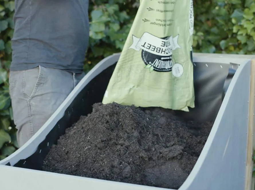 Person füllt Erde in Hochbeet