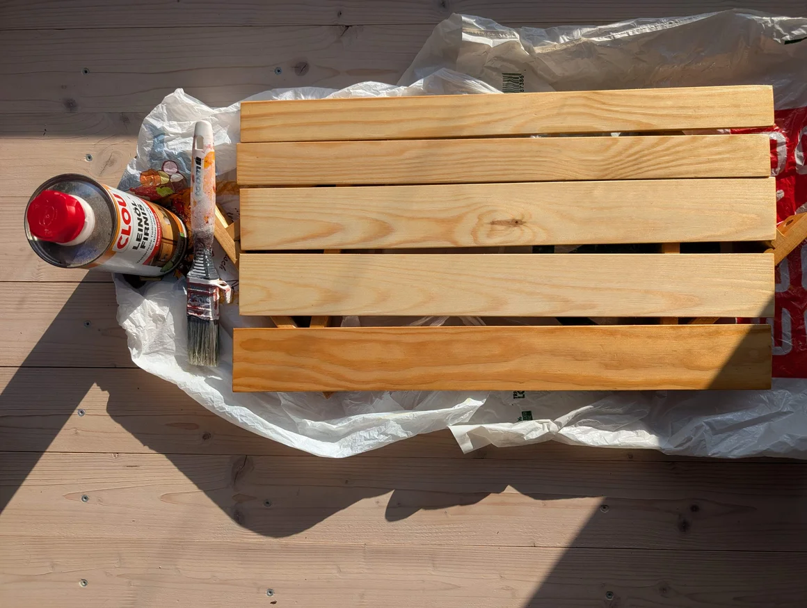 Ein Holzrost wird auf einer Folie mit einem Pinsel und Leinöl behandelt.