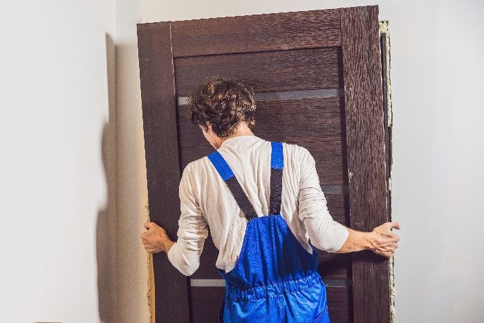 Mann hängt Holztüre in Türrahmen ein