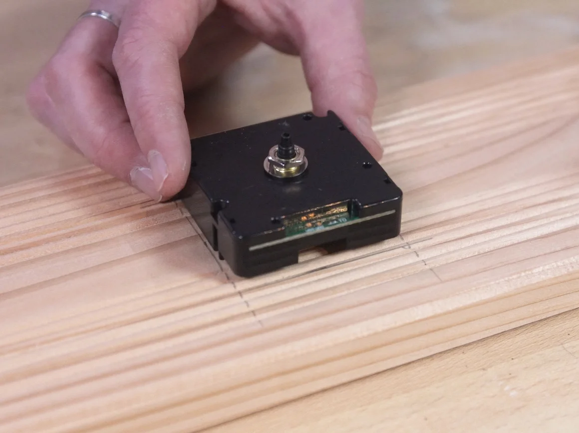 Person setzt Uhrwerk in Holzbrett ein