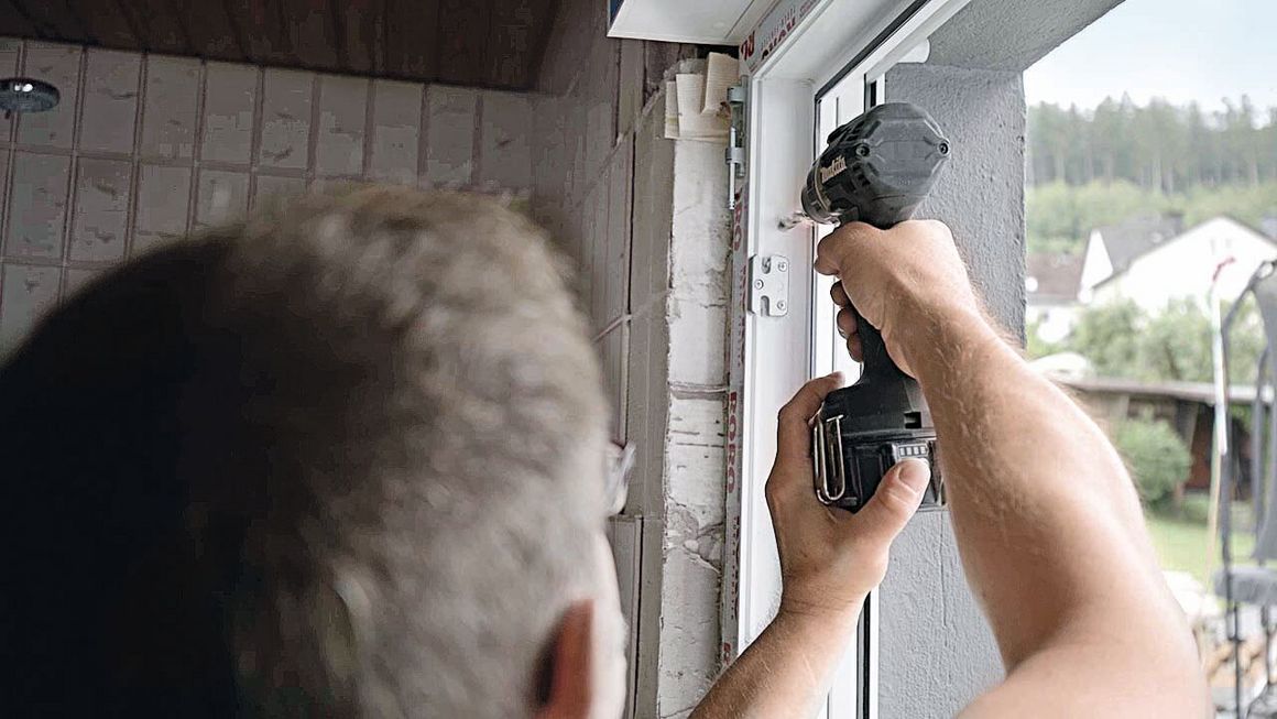 Ein Mann verschraubt einen Fensterrahmen mit der Wand
