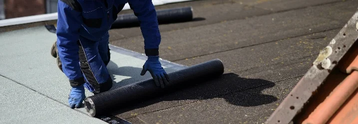 Person verlegt Dachpappe auf Dach.