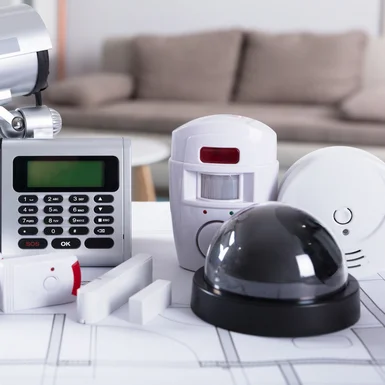 Eine Auswahl an Sicherheitssystemen für Zuhause, darunter eine Überwachungskamera, ein Bewegungssensor und eine Tastatur-Alarmanlage.