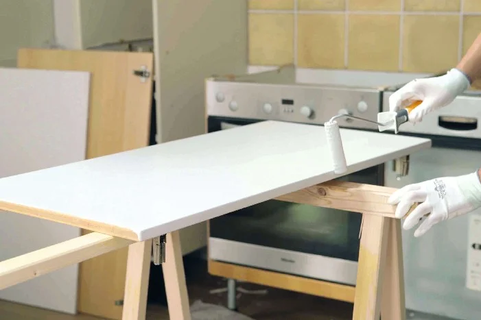 Person streicht Holzplatte mit Farbroller weiß