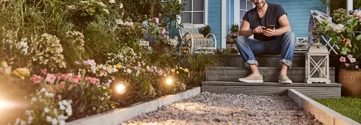 Person sitzt auf Holzterrasse im beleuchteten Garten