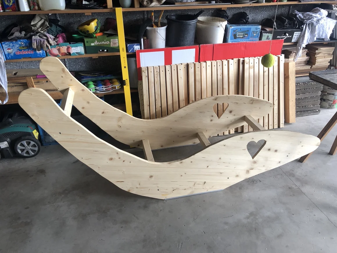 Zwei selbstgebaute Schaukelliegen aus Holz mit Herzausschnitt in einer Werkstatt.