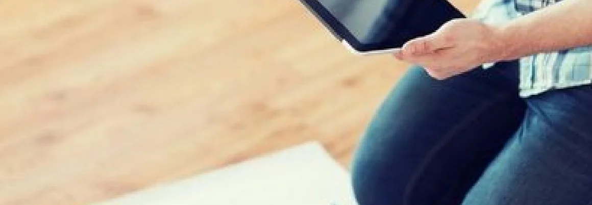 Person kniet auf Holzboden und betrachtet Tablet