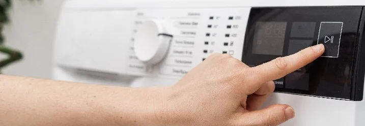 Hand betätigt eine Taste an einer Waschmaschine.