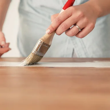 Person streicht Holztisch weiß.