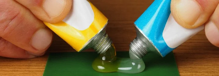 Zwei Tuben Klebstoff werden auf eine Fläche gedrückt.
