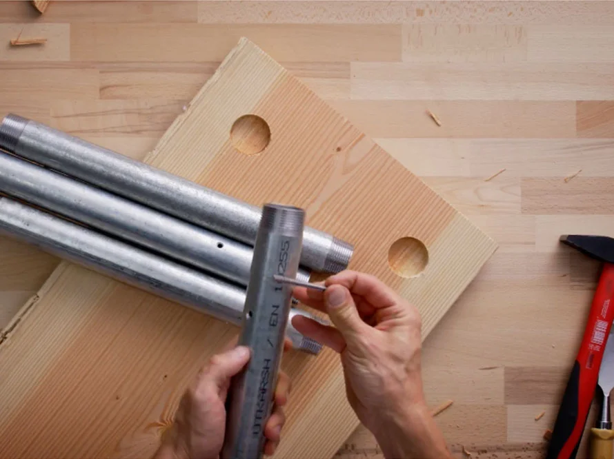 Person montiert Metallrohre auf Holzplatte