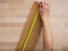 Person misst Holzbrett mit Zollstock ab
