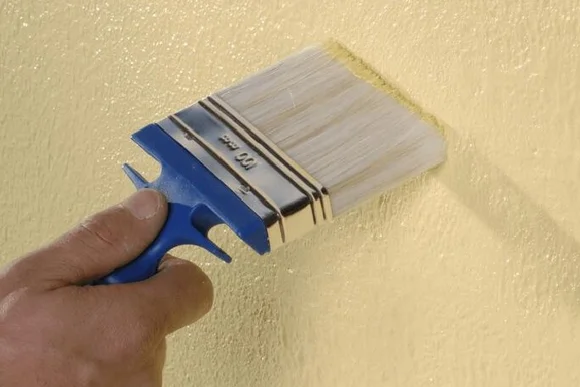 Hand streicht gelbe Farbe mit Pinsel an Wand