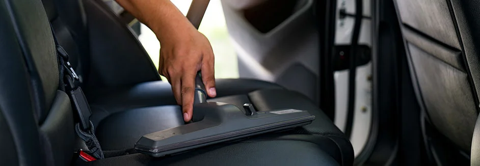 Hand reinigt Autositz mit Staubsauger