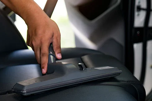 Hand reinigt Autositz mit Staubsauger