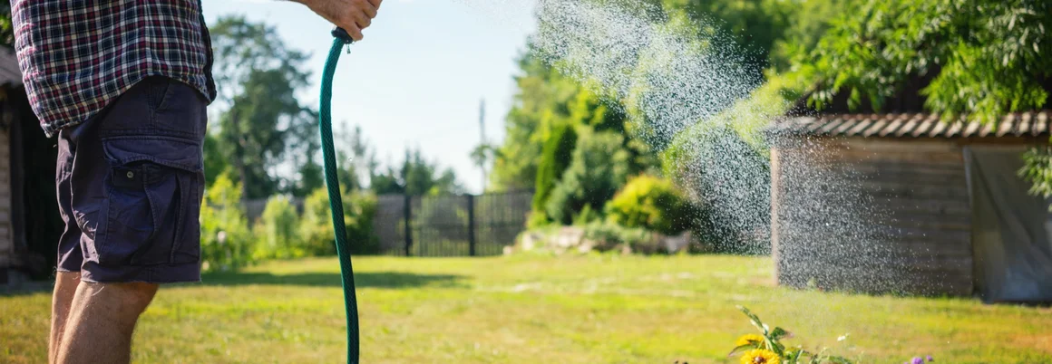 Person gießt Blumen mit Gartenschlauch