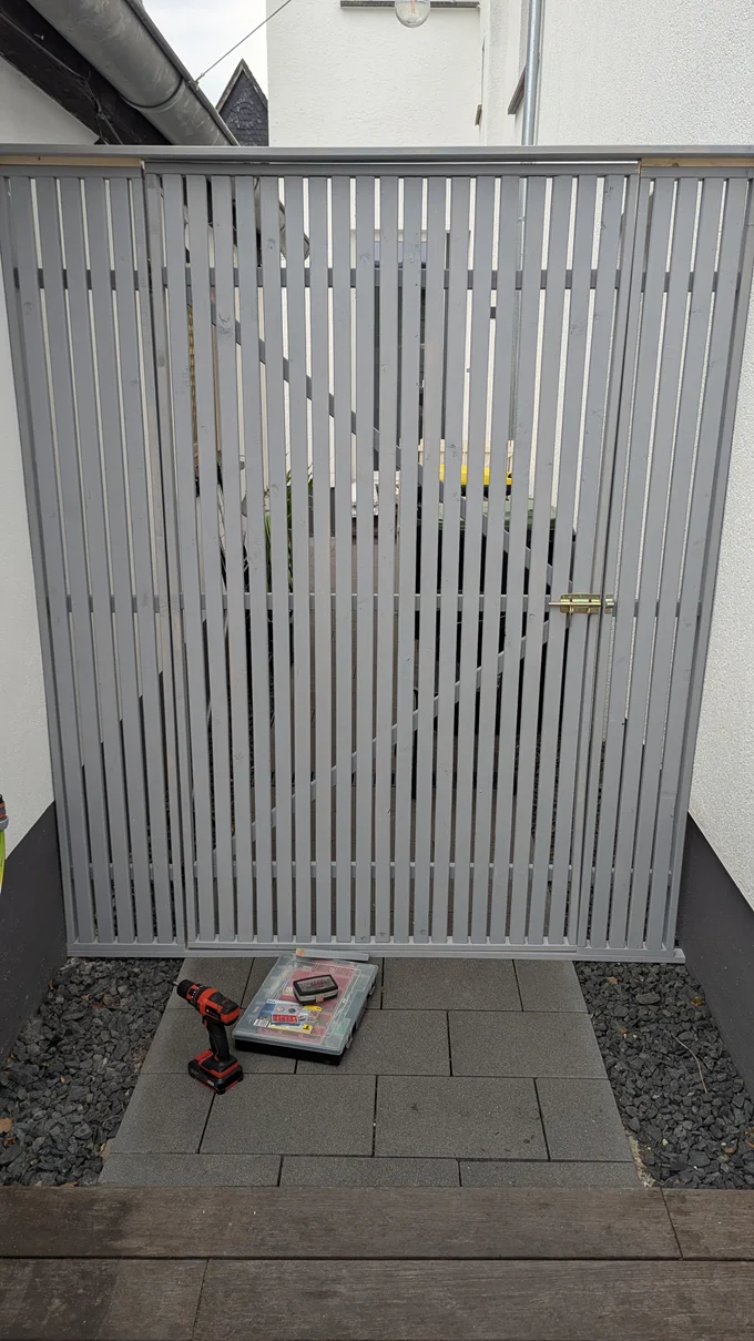 Akkuschrauber und Werkzeugkiste vor einem neu installierten, grauen Holztor.