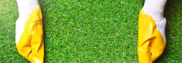 Hände mit Schutzhandschuhen halten Kunstrasen