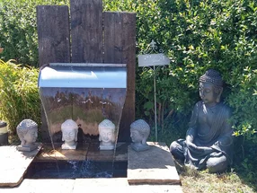 Gartenszene mit Buddhafiguren und einem Wasserspiel.