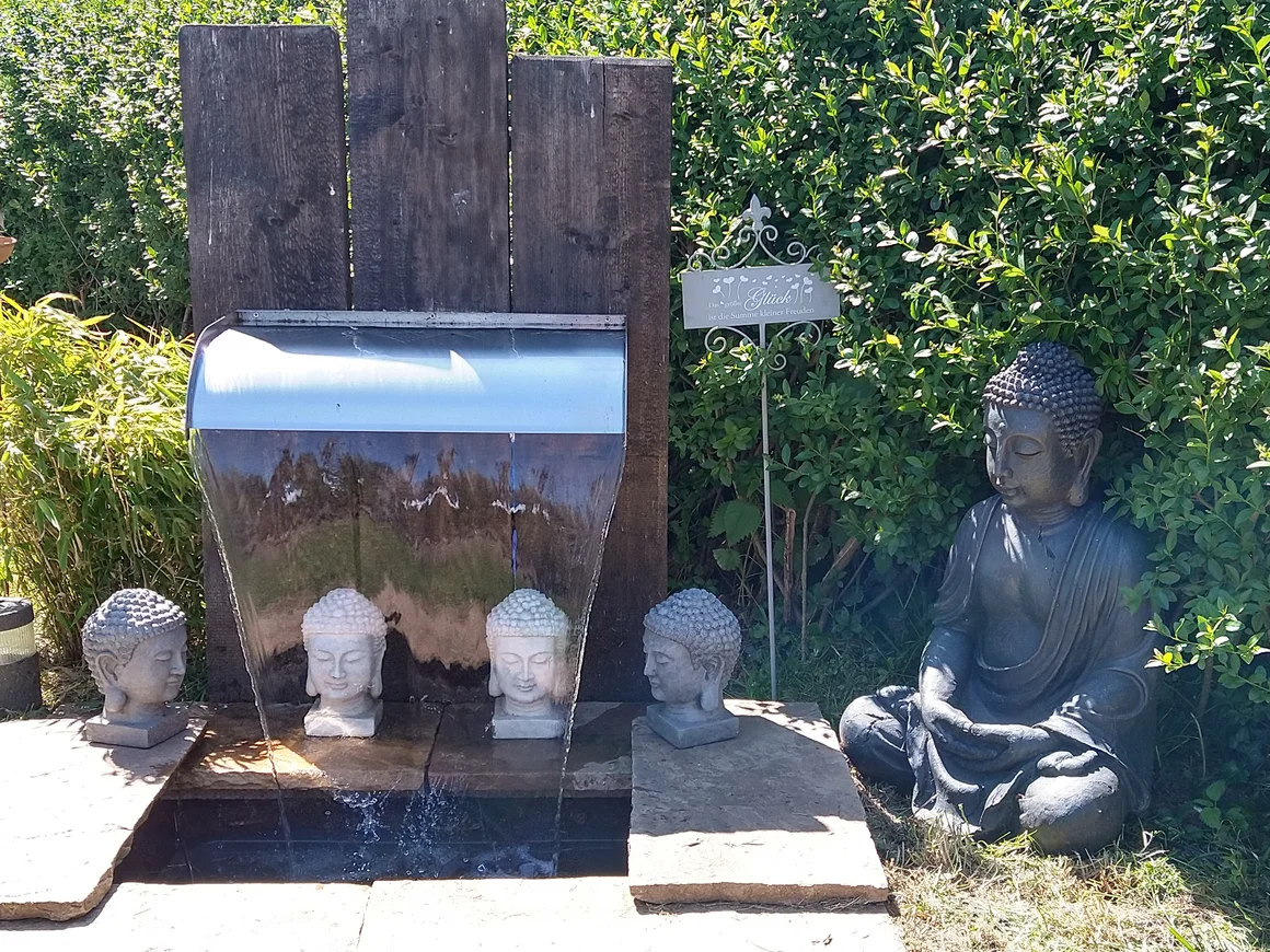 Gartenszene mit Buddhafiguren und einem Wasserspiel.