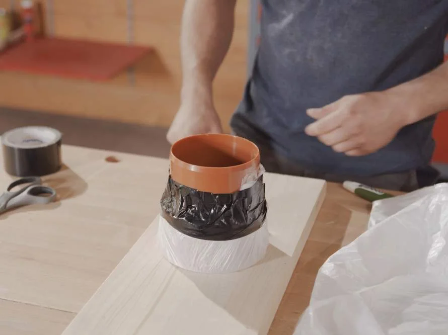 Ein orangenes Rohr wird mit Klebeband umwickelt.