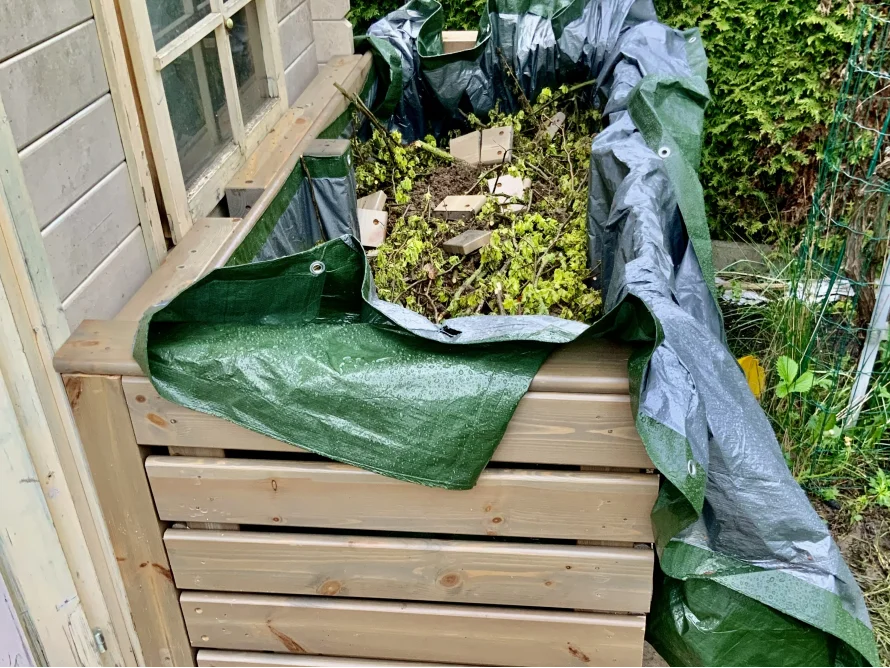 Kompost in einem Holzrahmen mit Plane abgedeckt