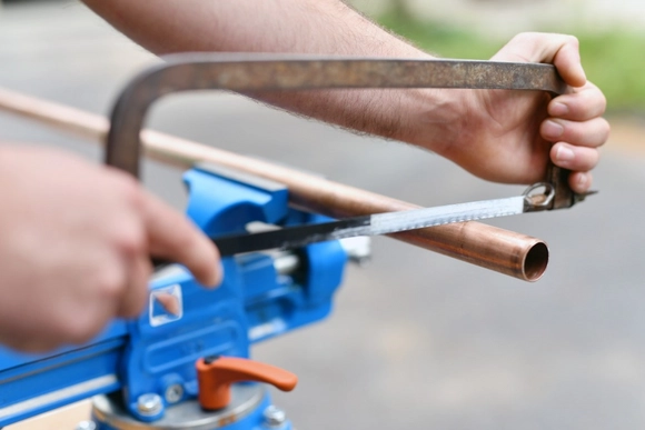 Eine Person sägt mit einer Metallsäge ein Kupferrohr in einem Schraubstock.