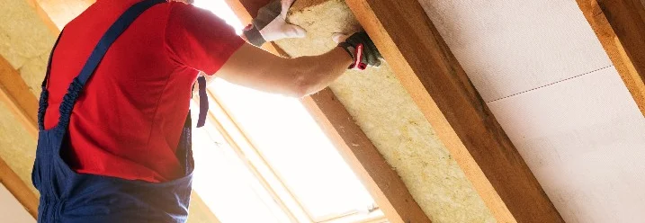 Person befestigt Dämmwolle am Dach.