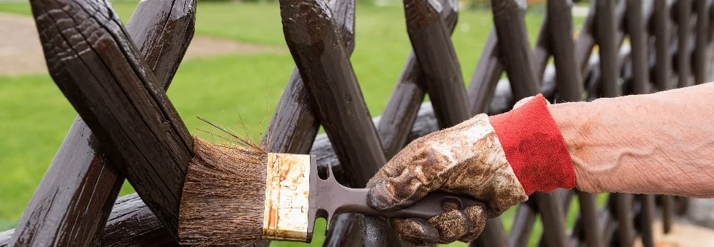 Person streicht Holzzaun mit Pinsel