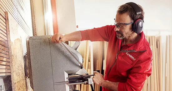 Ein Mensch mit Schutzausrüstung bedient eine große Säge für den Holzzuschnitt.