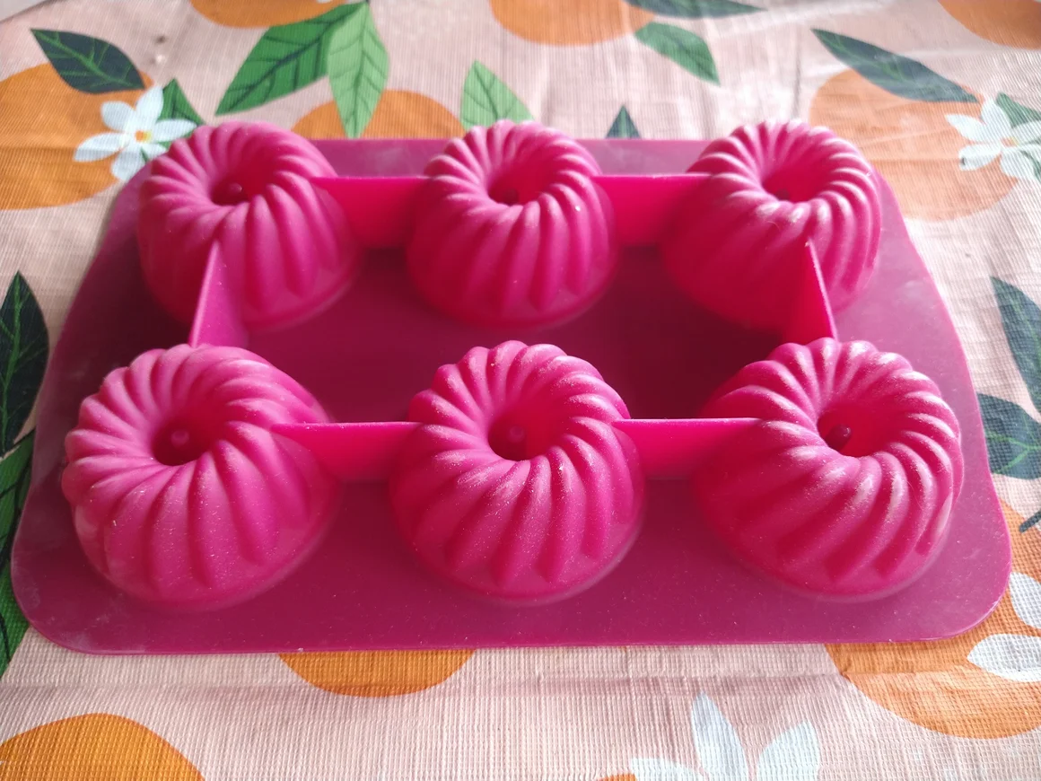 Eine rosa Silikon-Backform für sechs kleine Gugelhupf-Kuchen auf einer Tischdecke.