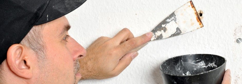 Ein Mann verspachtelt ein Bohrloch in einer weißen Wand.