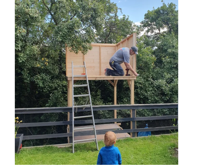 Person baut ein Gartenhaus. Ein Kind schaut zu.