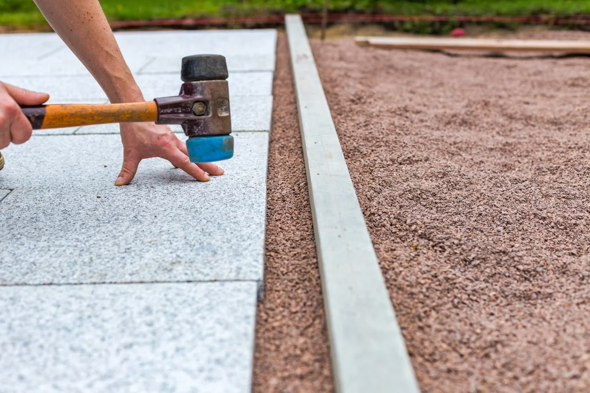 Person verlegt Granitplatten mit Gummihammer