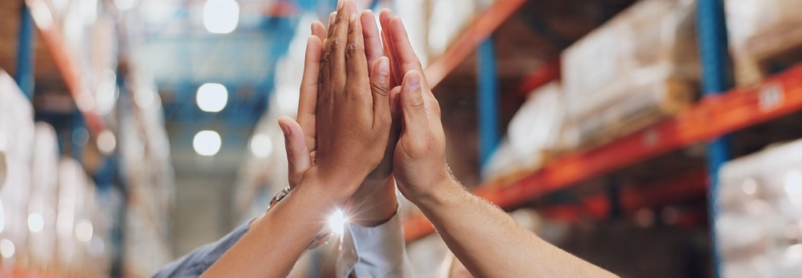 Mehrere Hände geben sich in einer Lagerhalle ein High-Five.