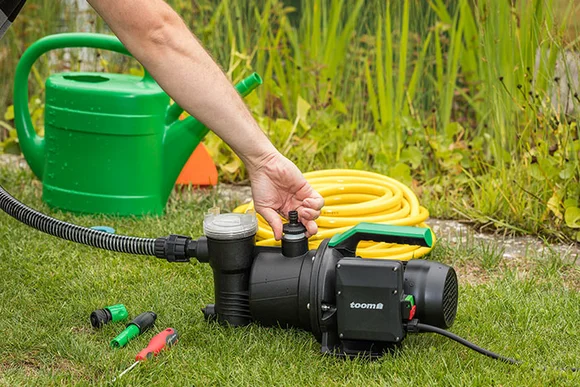 Person montiert Gartenpumpe auf Rasen.